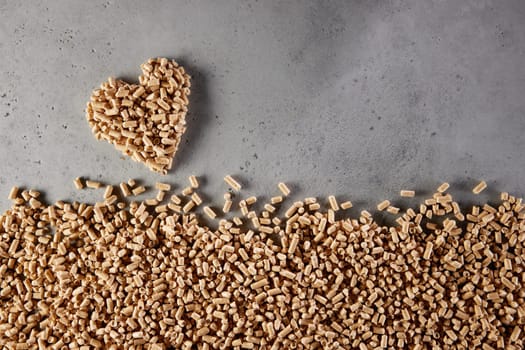 Top view of pile of solid fuel pellets scattered on gray background and forming heart