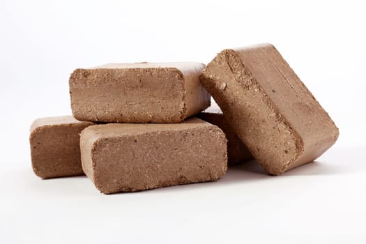 Pile of brown compressed peat biomass briquettes placed on each other on white surface in studio