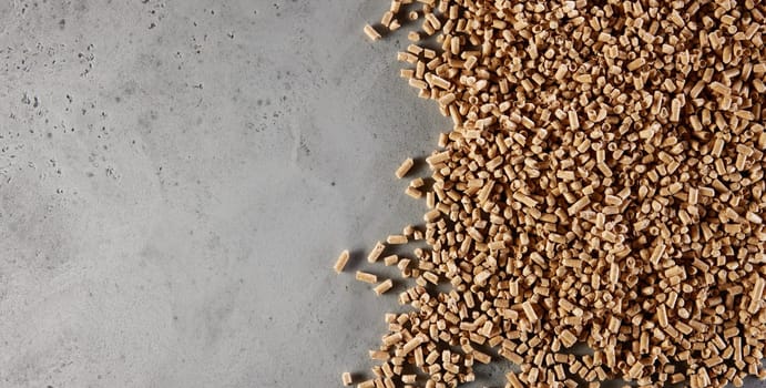 Top view of heap of natural brown fuel pellets scattered on gray concrete table