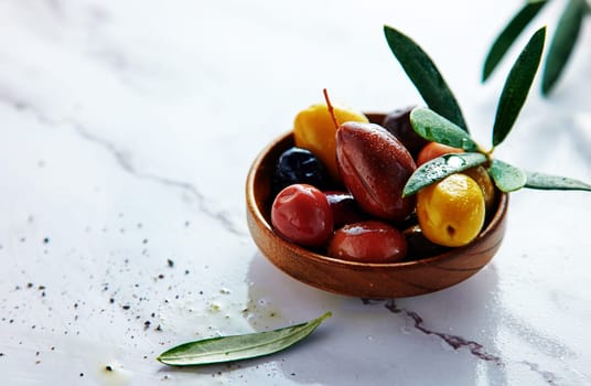 Assorted types of fresh pickled olives with leaves served in wooden bowl on white background with flavoring in light kitchen