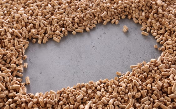 High angle of pile of chopped small wood pellets scattered on gray table in frame shape