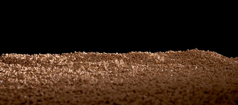 Heap of cylinder shaped solid fuel pellets scattered on surface against black background
