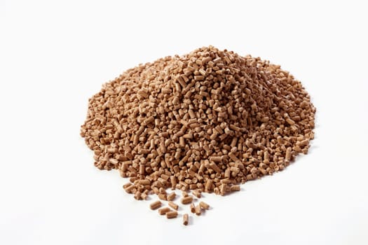 High angle of stack of dry chopped compressed wood pellets scattered on white background