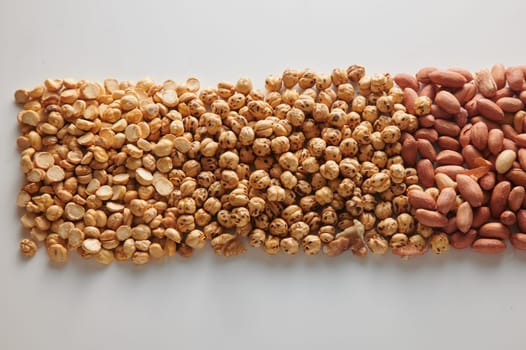 Top view heap of tasty hazelnuts with healthy unpeeled peanuts placed on white background in neat rows in light studio