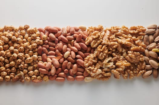 Top view pile of hazelnuts with unpeeled peanuts placed on clear white background with walnuts and pistachios in light studio