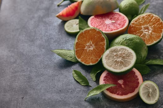 From above of various halved citrus fruits with lime and grapefruit placed on gray background with leaves in light room
