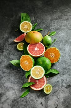 From above heap of ripe colorful exotic citrus fruits placed on gray background with green leaves in modern light studio