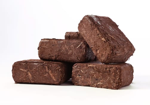 Pile of brown compressed biomass fuel briquettes placed on each other on white background