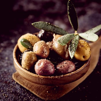 Bunch of assorted types of delicious pickled olives with seasoning and green leaves served on wooden spatula in light kitchen