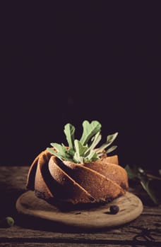 Delicious freshly baked cake made of fig decorated with green leaves served on wooden board against black background in kitchen