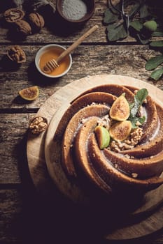 From above of sweet freshly baked fig cake served on wooden cutting board near walnuts and honey in light kitchen