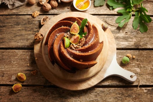 From above of appetizing homemade sweet fig cake with decorations served on wooden chopping board on table with nuts and honey
