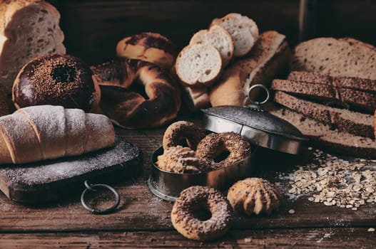 Assorted types of freshly baked buns and slices of Turkish bread served on table in kitchen of bakery with pastry