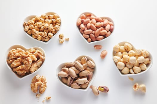 From above of assorted types of healthy nuts served on ceramic heart shaped bowls on white background in light studio