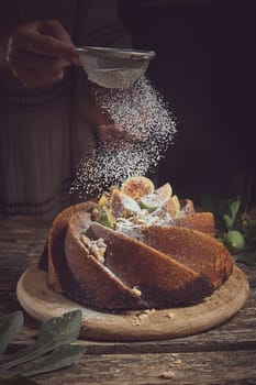 Crop anonymous cook sifting powdered sugar through sieve on sweet homemade fig cake served on cutting board in light kitchen