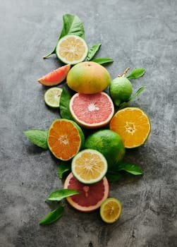 From above heap of slices and halves of limes with grapefruits and oranges served on gray background in light studio