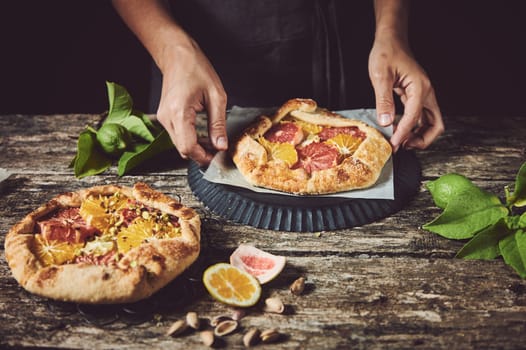 Crop anonymous cook taking sweet baked homemade fruity pastry with citrus fruits from parchment on baking pan at wooden table