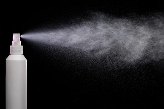 Spraying product in spray bottle over black background