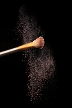 Make up brush with cosmetic powder splash, over black background. Splash image