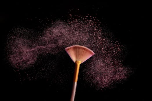 Make up brush with cosmetic powder splash, over black background. Splash image