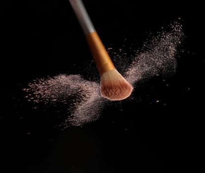 Make up brush with cosmetic powder splash, over black background. Splash image