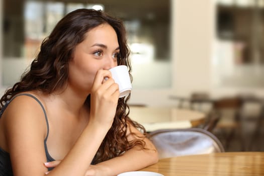 Happy woman drinking coffee in a restaurant looking away