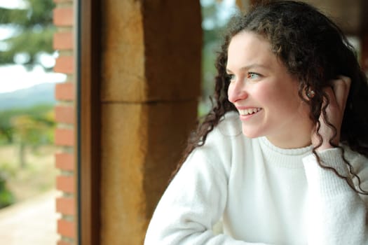 Happy female looks through a window sitting in a house interior