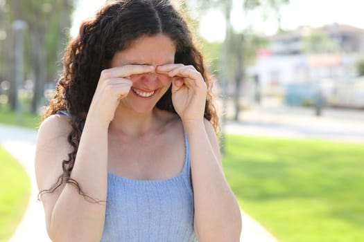 Stressed woman scratching itchy eyes while walks in a park