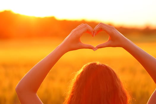 Close up of a woman doing heart shape in a field at sunset