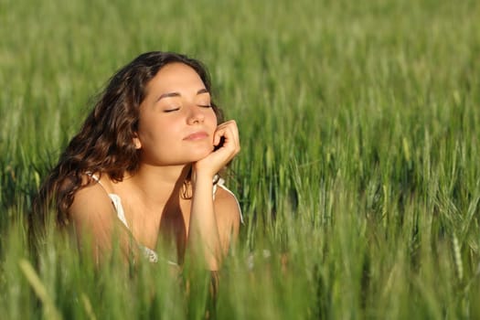 Woman breathing fresh air and relaxing in a green wheat field