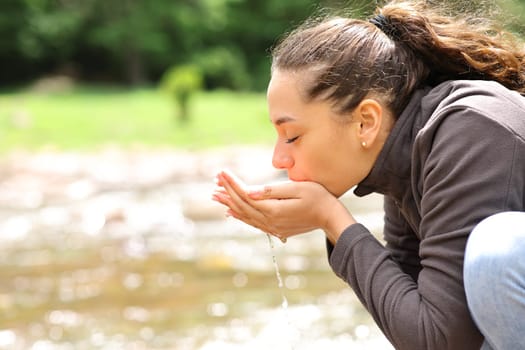 Side view portrait of a woman drinking water from river in the mountain