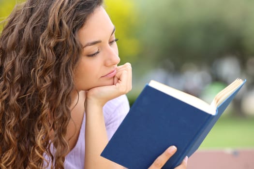 Relaxed woman reading a book sitting in a park alone