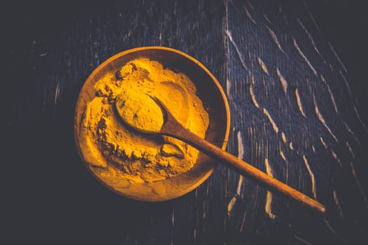 Indian turmeric powder, curcuma spice in small bowl with spoon, Haldi powder on wooden background