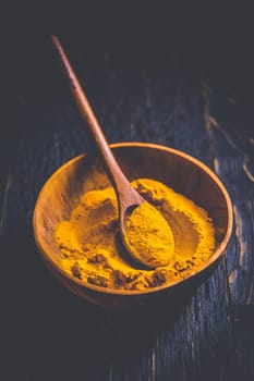 Indian turmeric powder, curcuma spice in small bowl with spoon, Haldi powder on wooden background