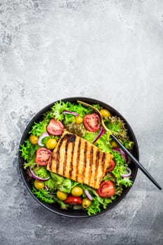 Fresh salad with grilled cheese, tomatoes and olives on grey
