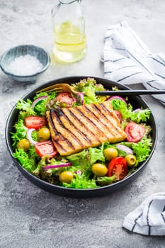 Fresh salad with grilled cheese, tomatoes and olives on grey