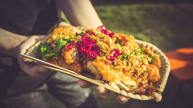 Street food - Hand holding portion of spicy chicken wings with red cabbage and herbs