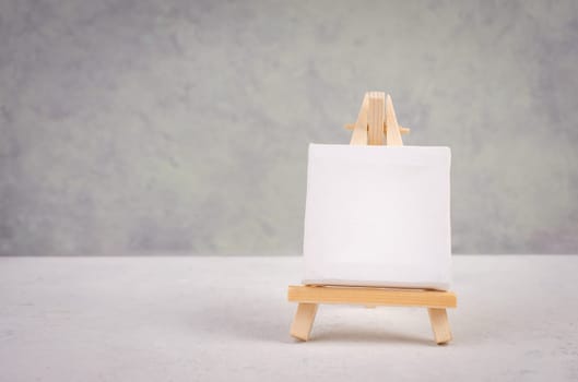 Easel with blank white canvas in front of a gray textured background, frame to add paintings and pictures