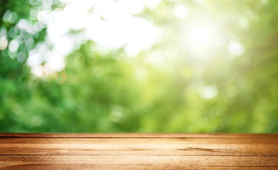 Blank country fence plank, table top or counter bar with abstract green forest trees background. Nature bokeh sunlight. Mock up, product template. Banner or header for advertise on social media