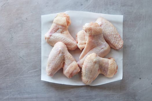 Top view heap of uncooked chicken wings with skin placed on napkin on gray background in light kitchen during cooking preparation