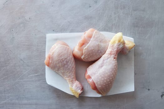 Top view of uncooked chicken drumsticks on napkin placed on gray background in light kitchen during cooking preparation at home
