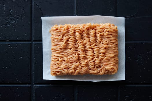 Top view of uncooked fresh chicken ground meat placed on napkin on black background in light kitchen during cooking preparation