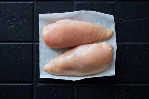 Top view of raw chicken breasts on napkin placed on black background in light kitchen during cooking preparation at home
