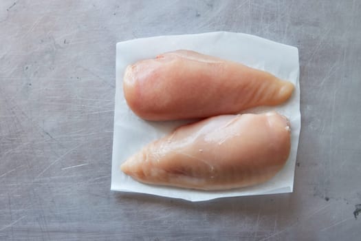 Top view of uncooked fresh chicken breasts on white napkin placed on gray background in light kitchen during cooking process