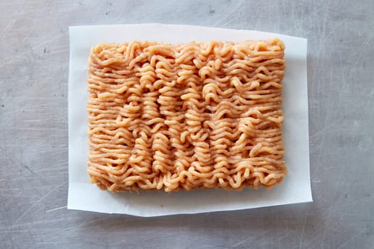 Top view of raw fresh chicken mince in white napkin placed on gray background in light kitchen during cooking process