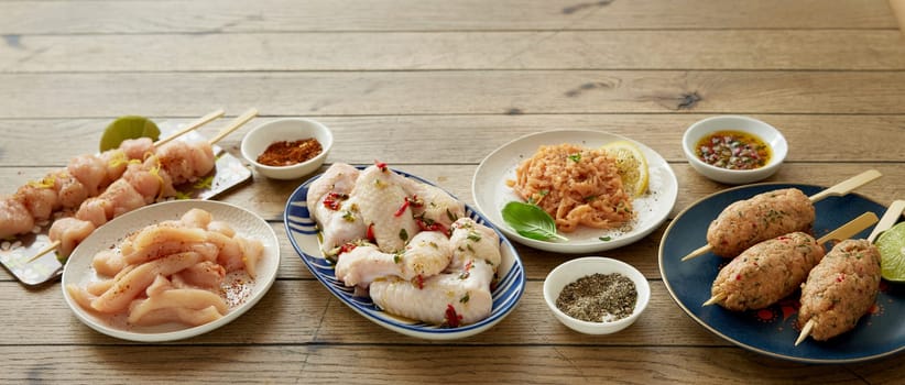 From above different types of uncooked chicken meat served on wooden table with various spices in light kitchen during cooking process