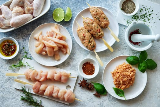 Top view of raw chicken skewers and lula kebab served on gray background with uncooked strips and wings in kitchen