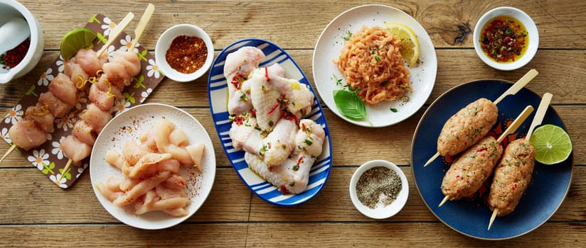 Top view mix of uncooked chicken meat served on plates on wooden table with assorted spices and condiments in kitchen