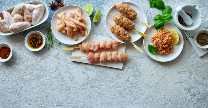 From above of assorted uncooked chicken meat served on gray background with mix of spices and greens in light kitchen