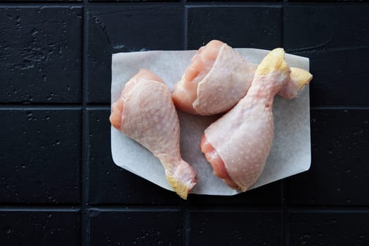Top view heap of fresh chicken drumsticks with skin placed on clear black background in light kitchen during cooking preparation
